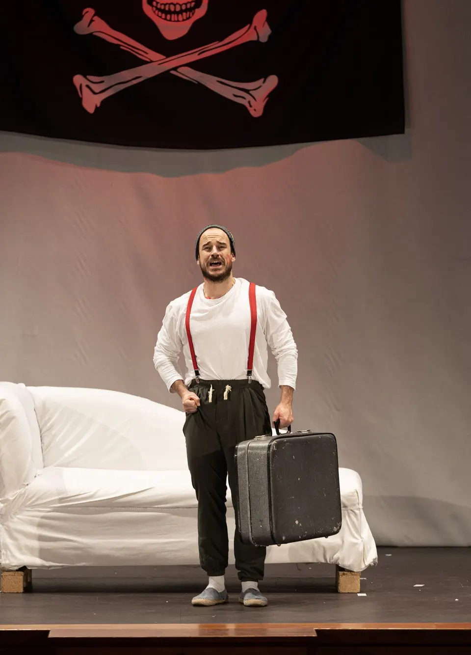 Charlie en escena con una maleta, bajo una bandera pirata