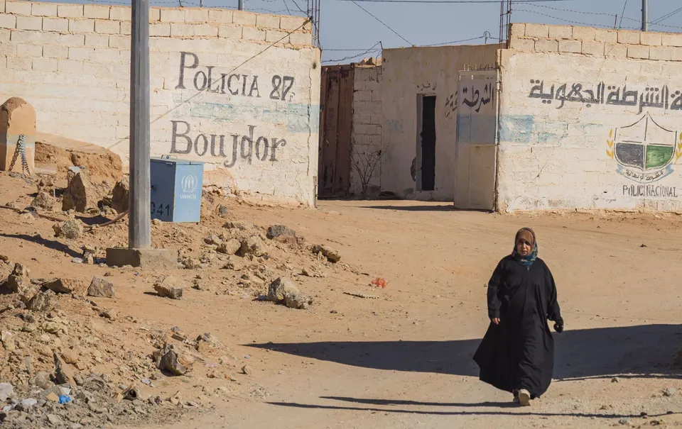 Una mujer con melfa camina por una calle de tierra de Bojador, entre casas bajas