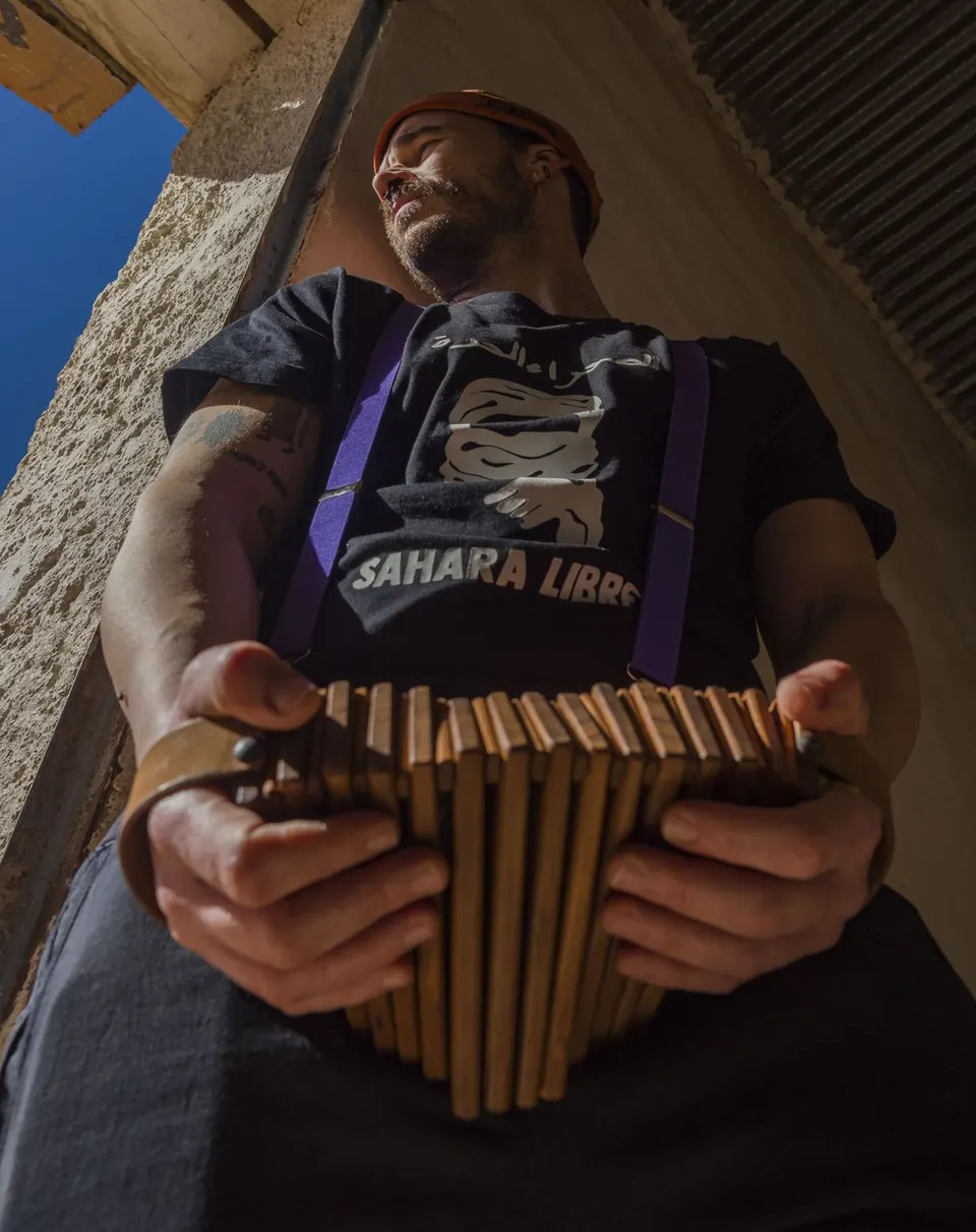 Un mago, visto desde abajo, toca un instrumento de fuelle con una camiseta de «Sahara Libre»