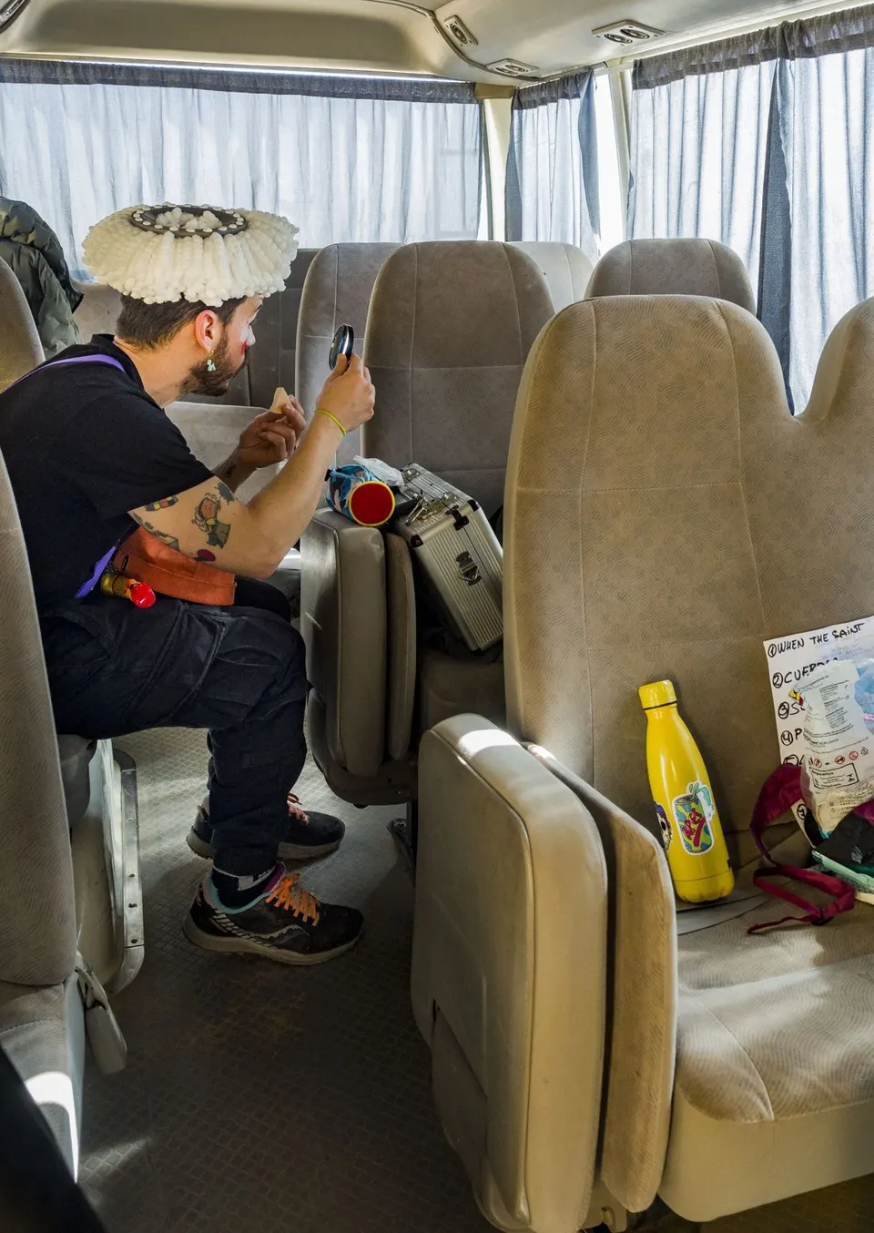 Un mago mira el móvil en el asiento de un autobús, junto a una peluca blanca